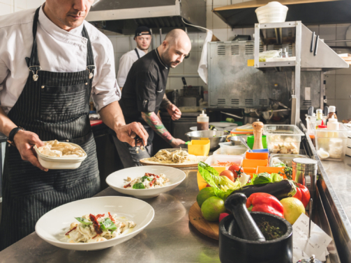 Professional chef cooking in the kitchen restaurant at the hotel, preparing dinner. A cook in an apron makes a salad of vegetables and pizza