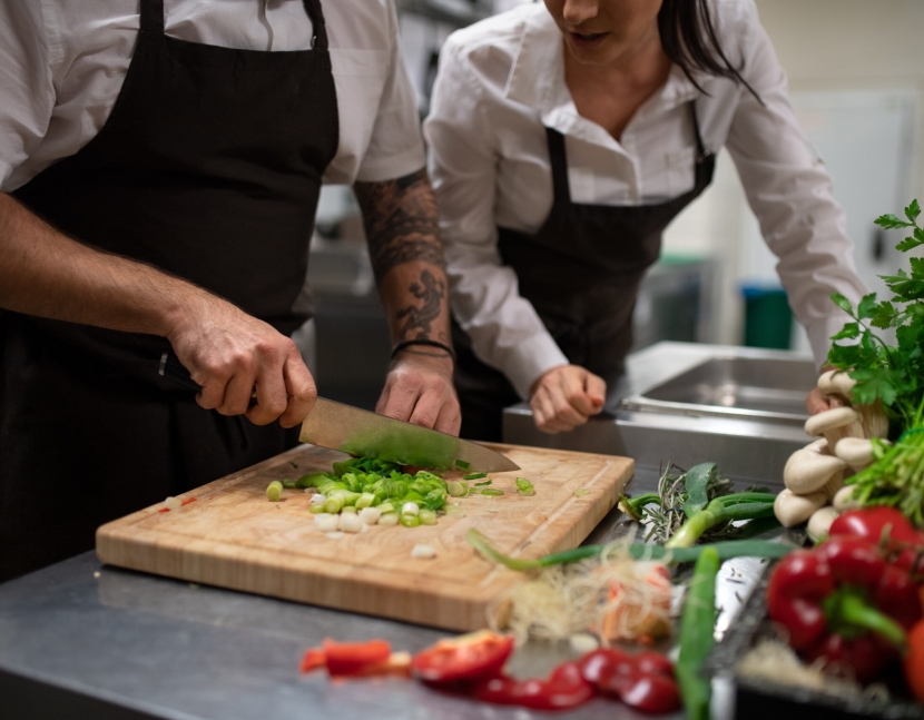 A chef teaching how to cook, cutting vegetables indoors in commercial kitchen.